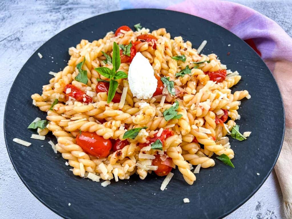 Pasta with tomatoes and basil on a black plate.