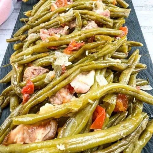 Green beans with meat and tomatoes on a black plate.