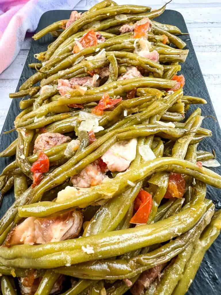 Green beans with meat and tomatoes on a black plate.