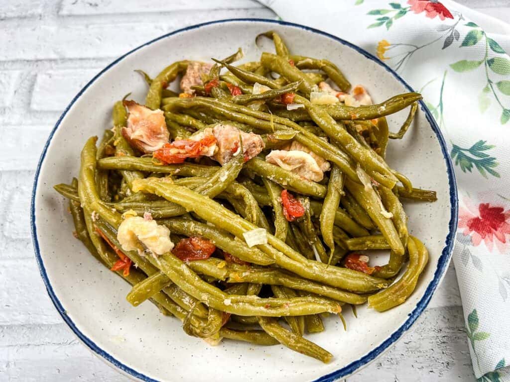 Green beans in a white bowl with tomatoes.