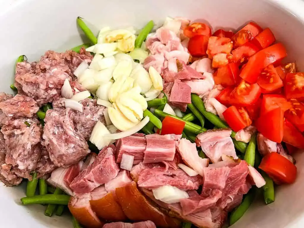 Ham, green beans, tomatoes and onions in a white bowl.