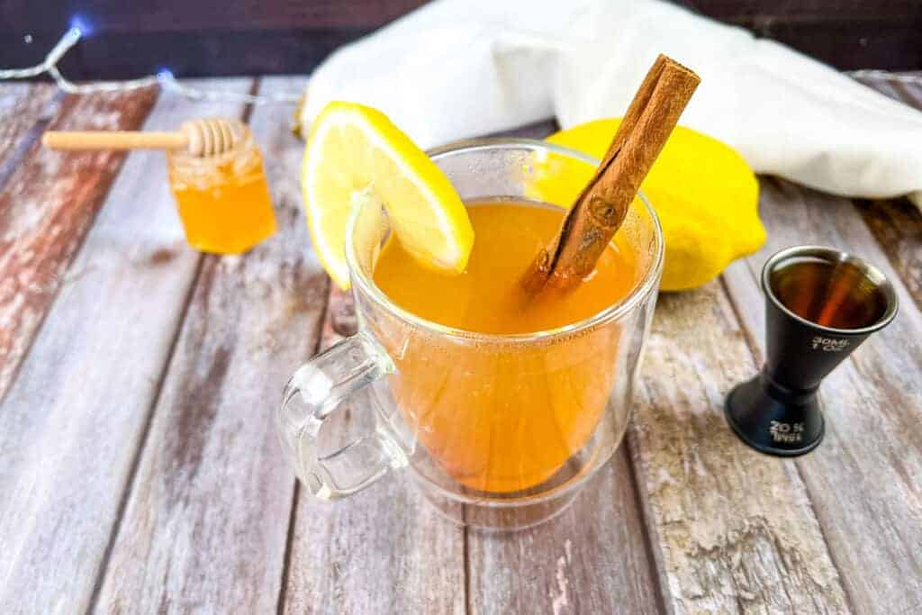 A mug of hot apple cider with cinnamon sticks and lemon slices.