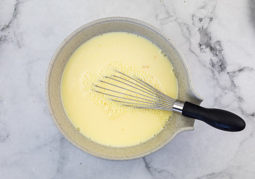 A bowl of egg yolks with a whisk in it.