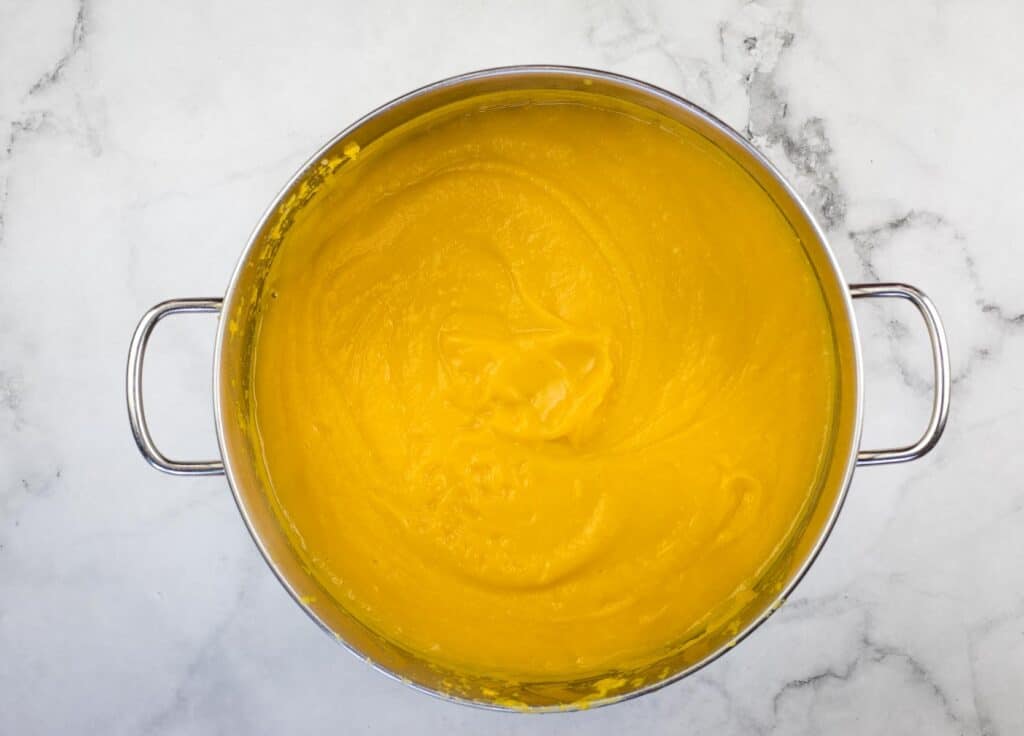 A pot of yellow soup on a marble countertop.