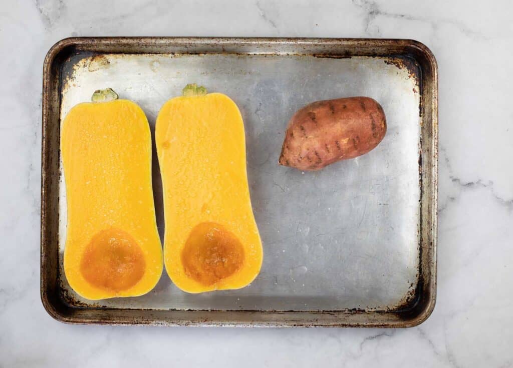 Two squashes and a sweet potato on a baking sheet.