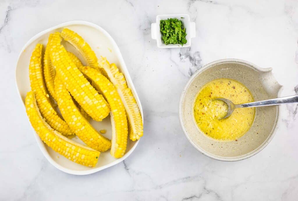 Corn on the cob in a bowl next to a bowl of sauce.