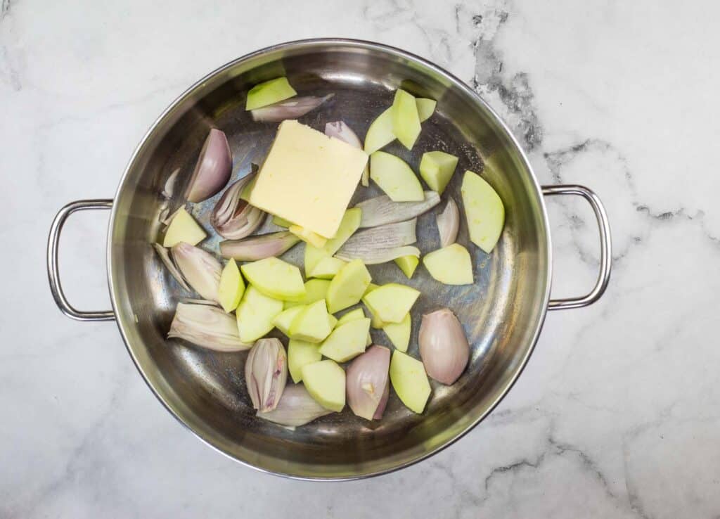 Sliced onions and butter in a pan on a marble countertop.