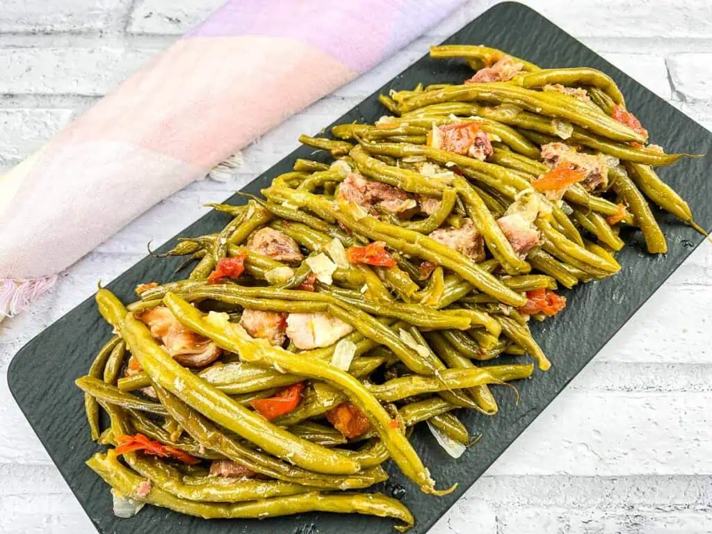 Green beans with ham and peppers on a black plate.