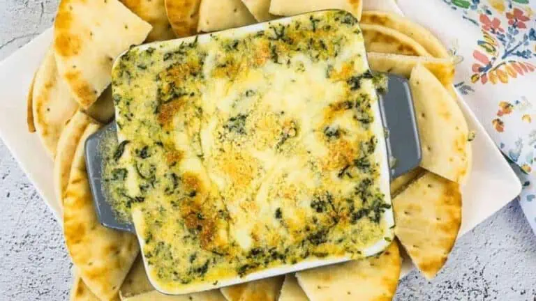 Spinach dip with crackers on a white plate.