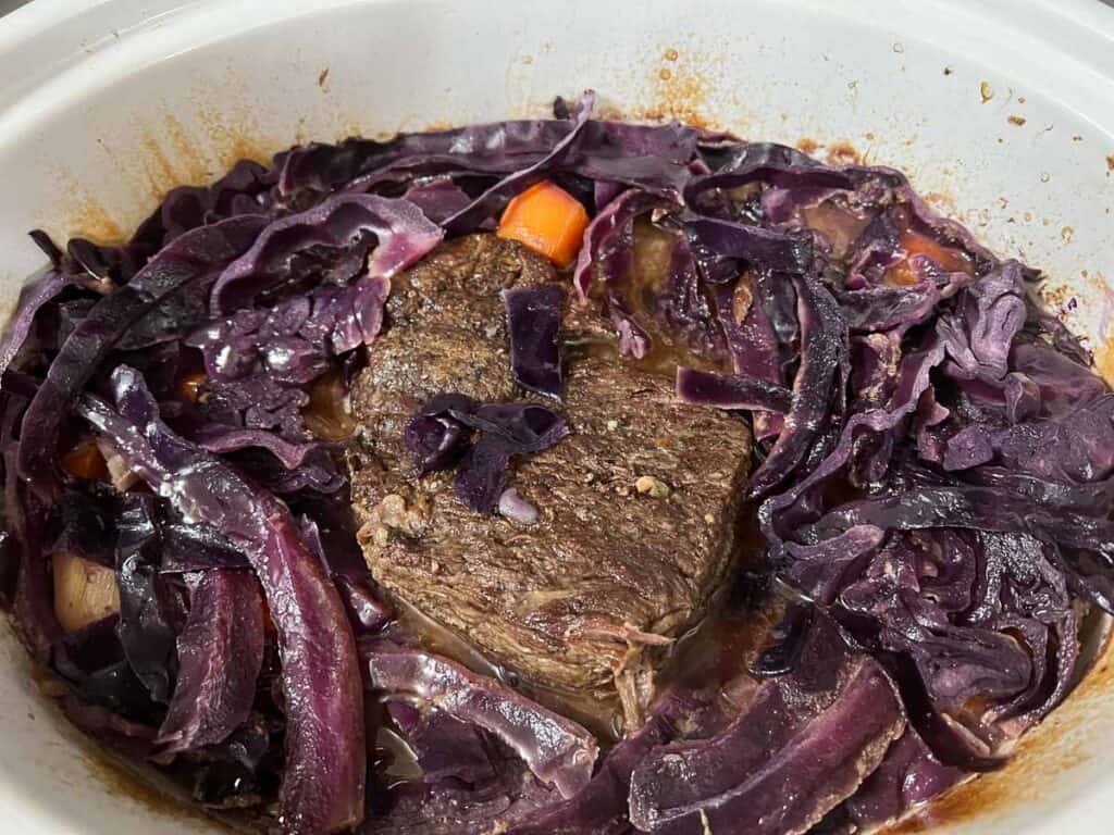 A crock pot full of meat and red cabbage.