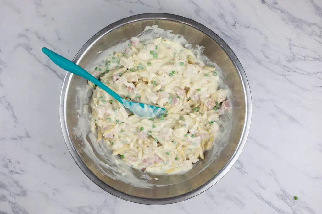 Ham and cheese pasta in a bowl with a blue spoon.