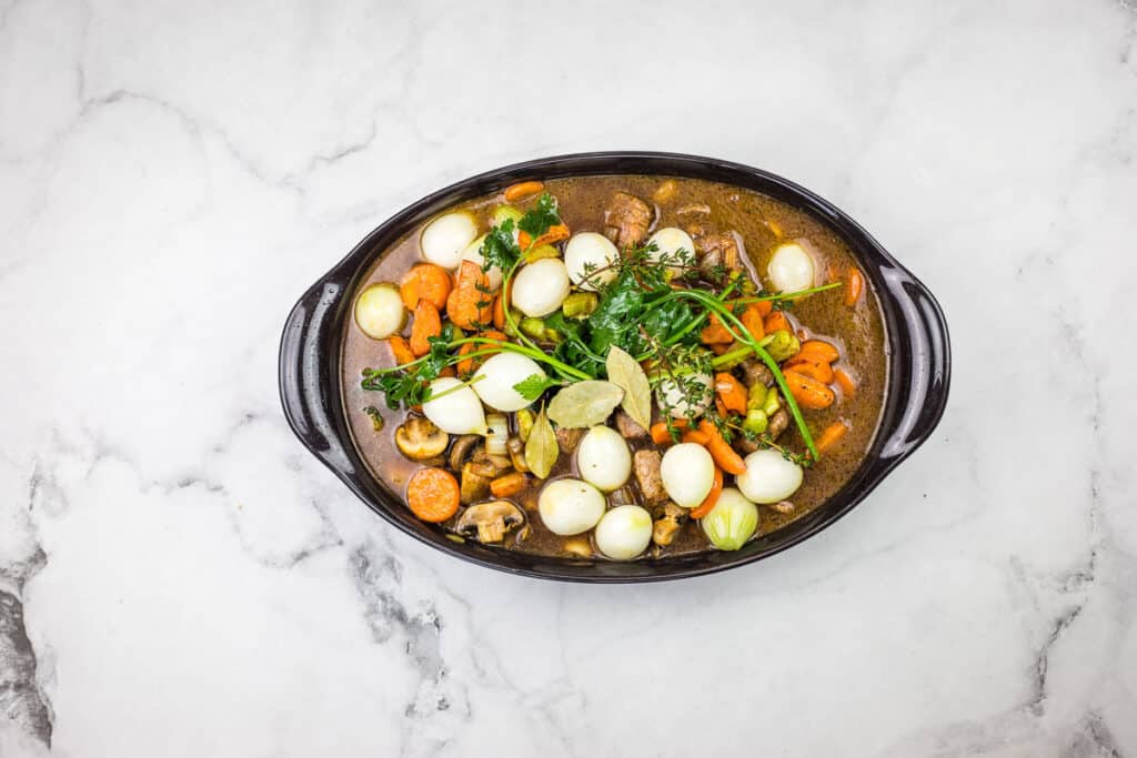 A bowl of stew with carrots, onions and mushrooms.