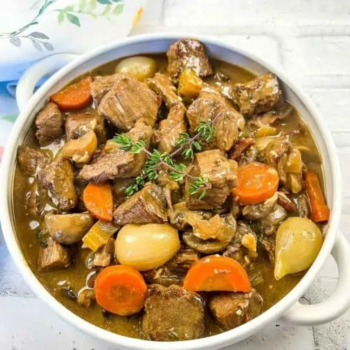 Beef stew in a white bowl with carrots and thyme.