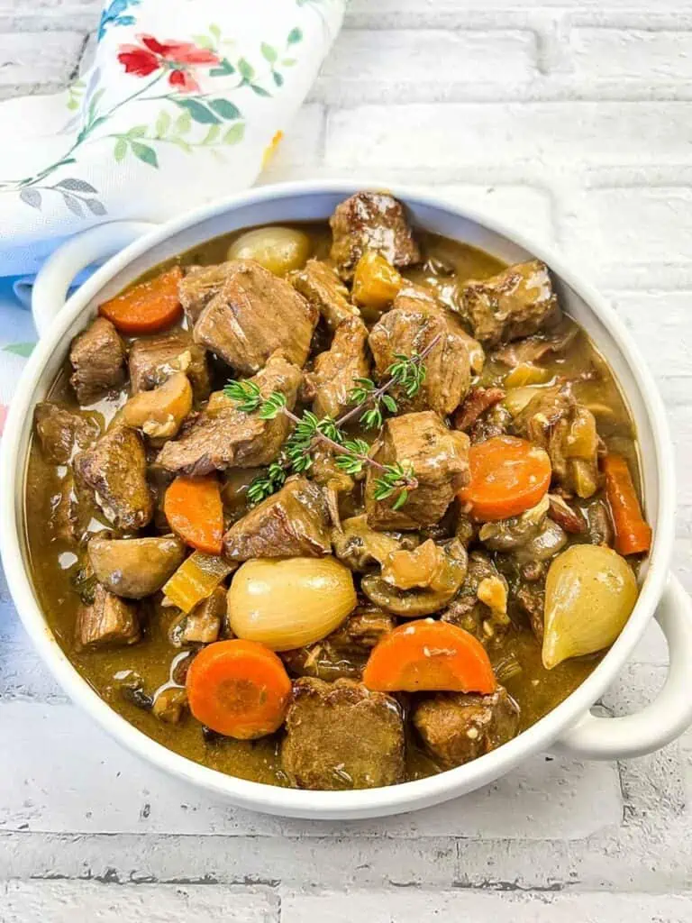 Beef stew in a white bowl with carrots and thyme.