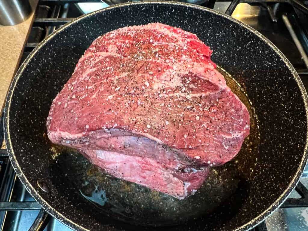 A piece of meat in a frying pan on a stove.