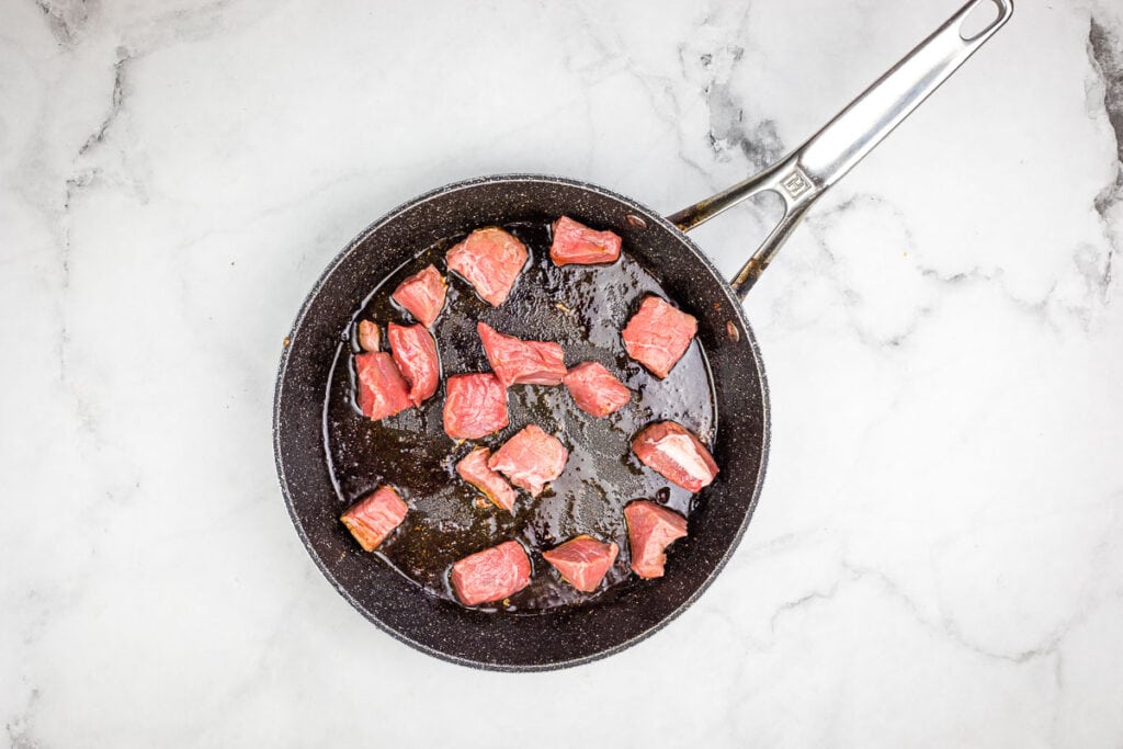Beef in a frying pan on a marble countertop.