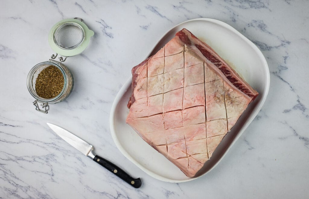 A New York strip roast on a plate next to a knife.