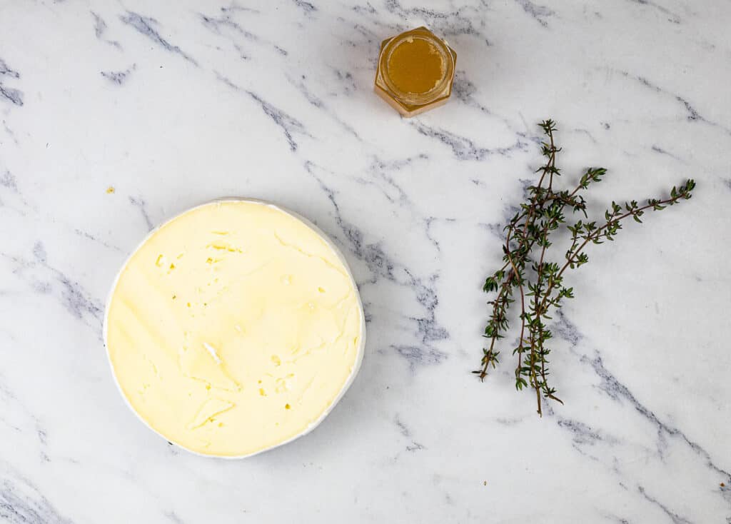 A bowl of butter on a marble table next to a jar of honey and a sprig of thyme.