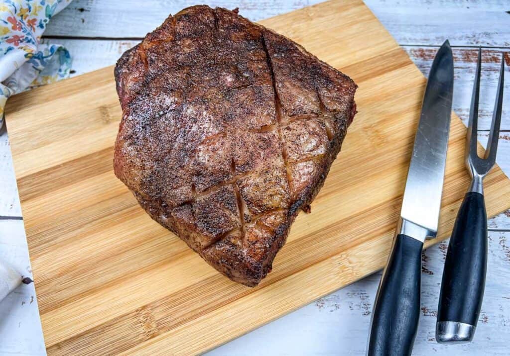 Smoked New York Strip Roast on a cutting board with a knife and fork.