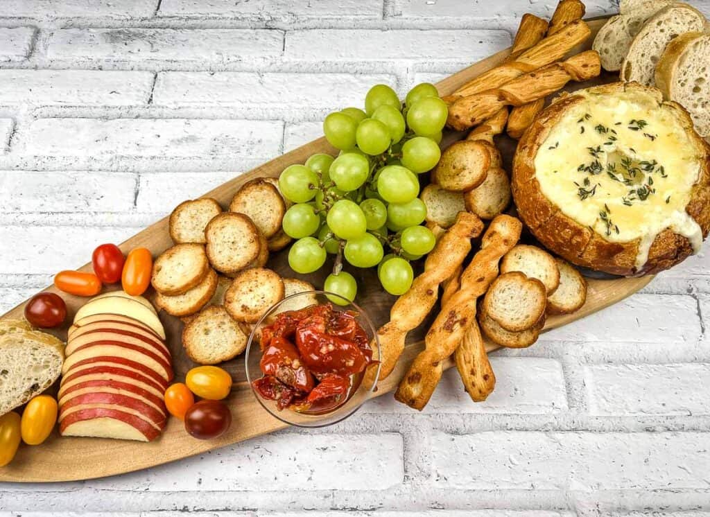 A wooden platter with cheese, crackers, grapes and grapes.