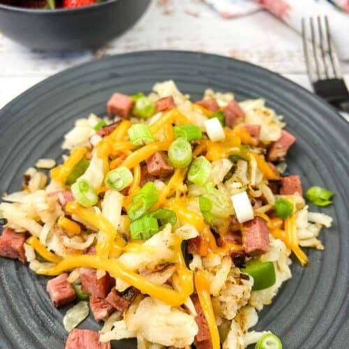 A plate with Montreal Smoked Meat Hash with strawberries in the background.