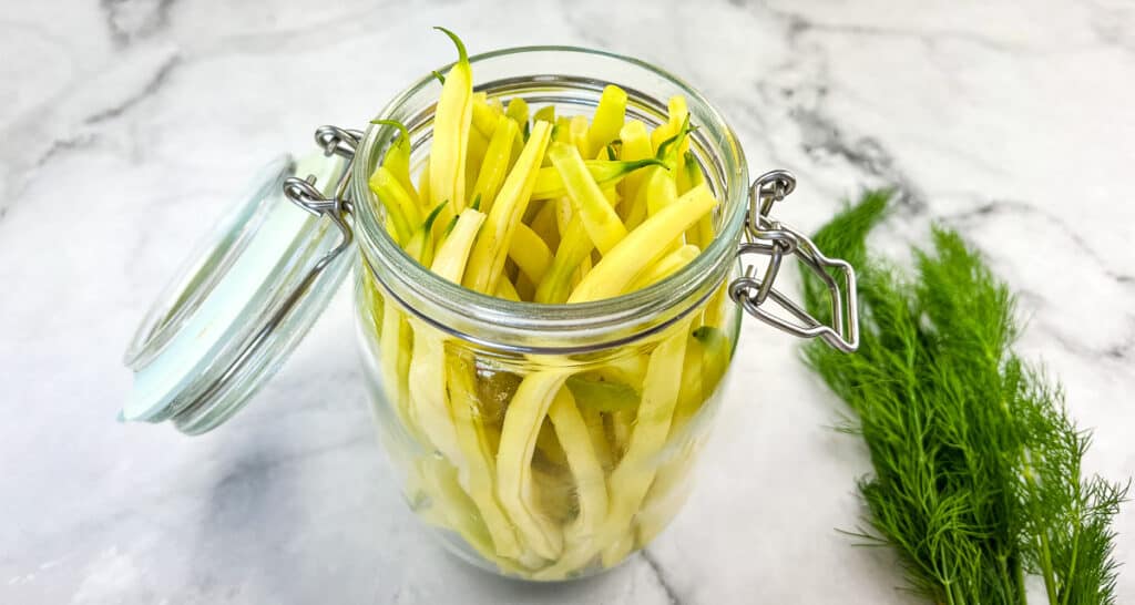 A glass jar filled with green beans and dill.