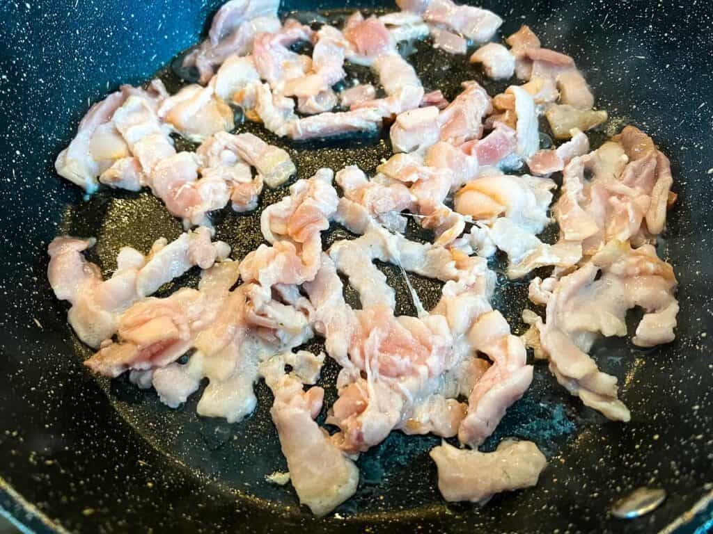 Bacon in a frying pan on a stove top.