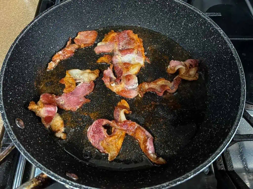 Fried bacon in a frying pan on a stove.