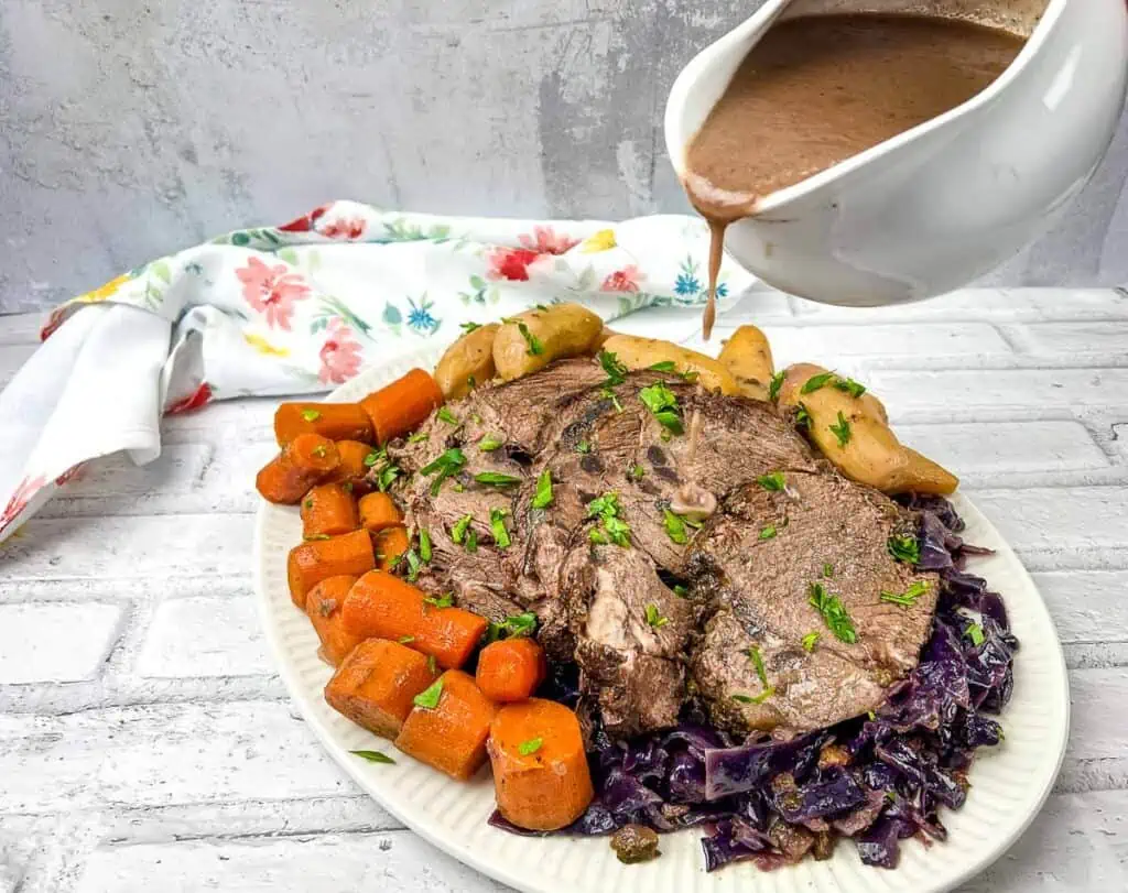 A plate of roast beef with a sauce being poured over it.