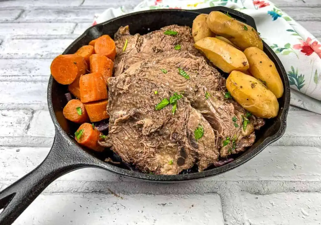 A cast iron skillet with roast beef, carrots and potatoes.