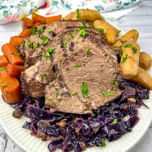 Roast beef with red cabbage and potatoes on a white plate.