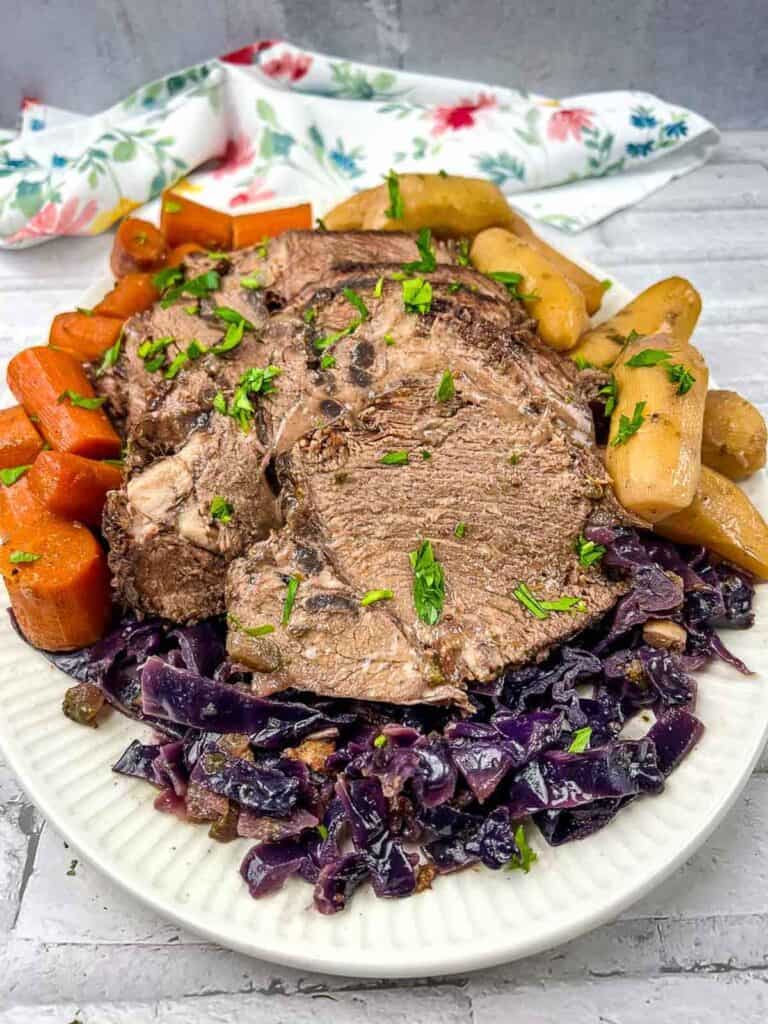 Roast beef with red cabbage and potatoes on a white plate.