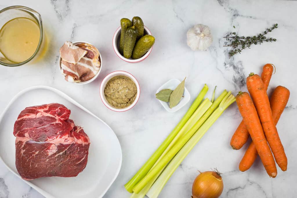 A plate of meat, carrots, celery and other ingredients on a marble table.