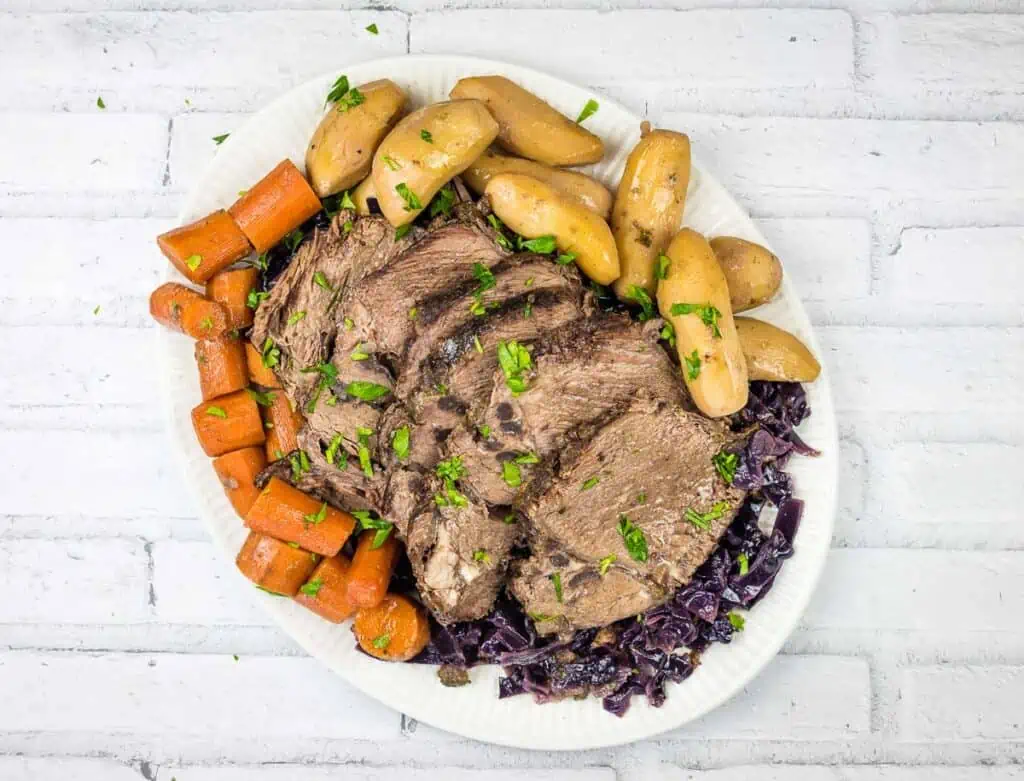 A plate with a roast, potatoes and red cabbage.