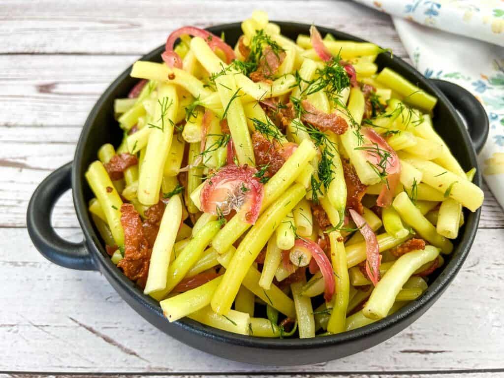 A bowl of German Yellow Beans and bacon salad on a wooden table.