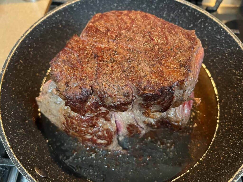 A pot roast being browned in a frying pan.