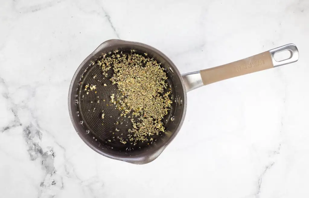 A pan with spices in it on a marble surface.