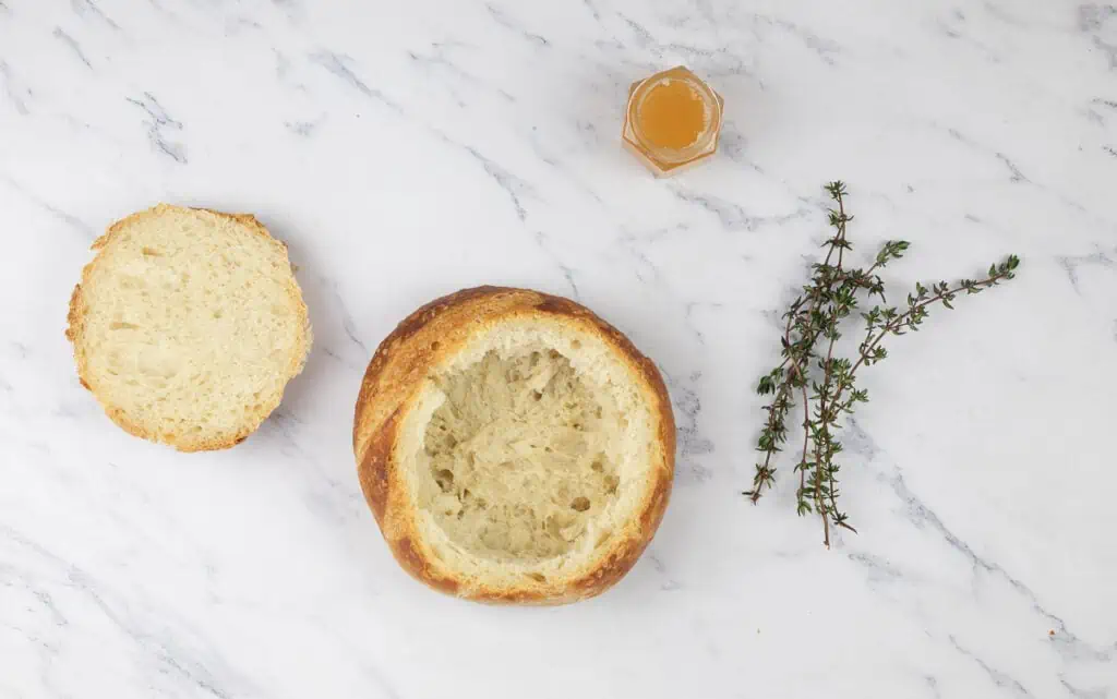 A loaf of bread with a sprig of thyme and a bottle of honey.