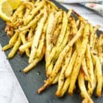 Air Fryer Lemon Pepper Yellow Beans on a black plate with lemon wedges.