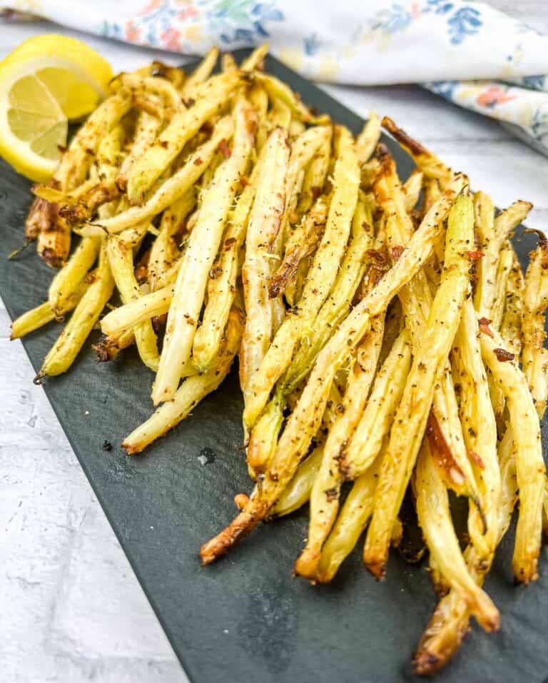 Air Fryer Lemon Pepper Yellow Beans on a black plate with lemon wedges.