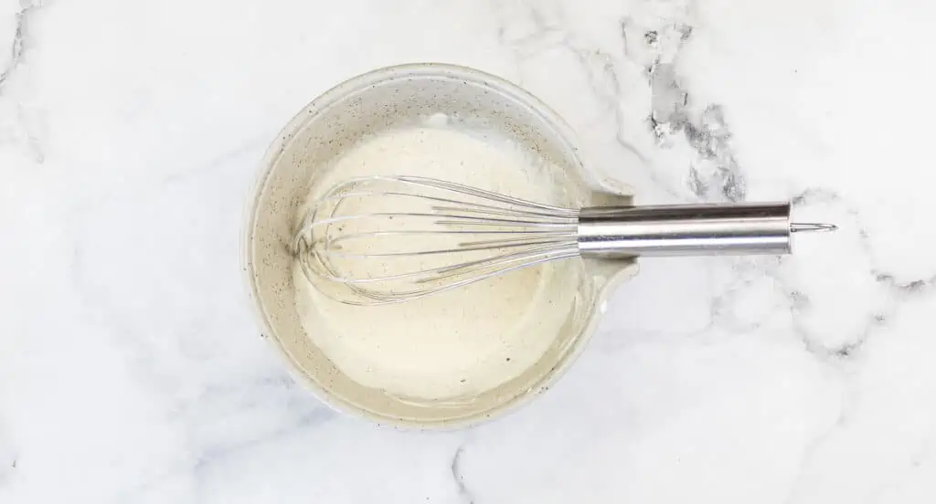 A white bowl with a whisk and the dressing in it.