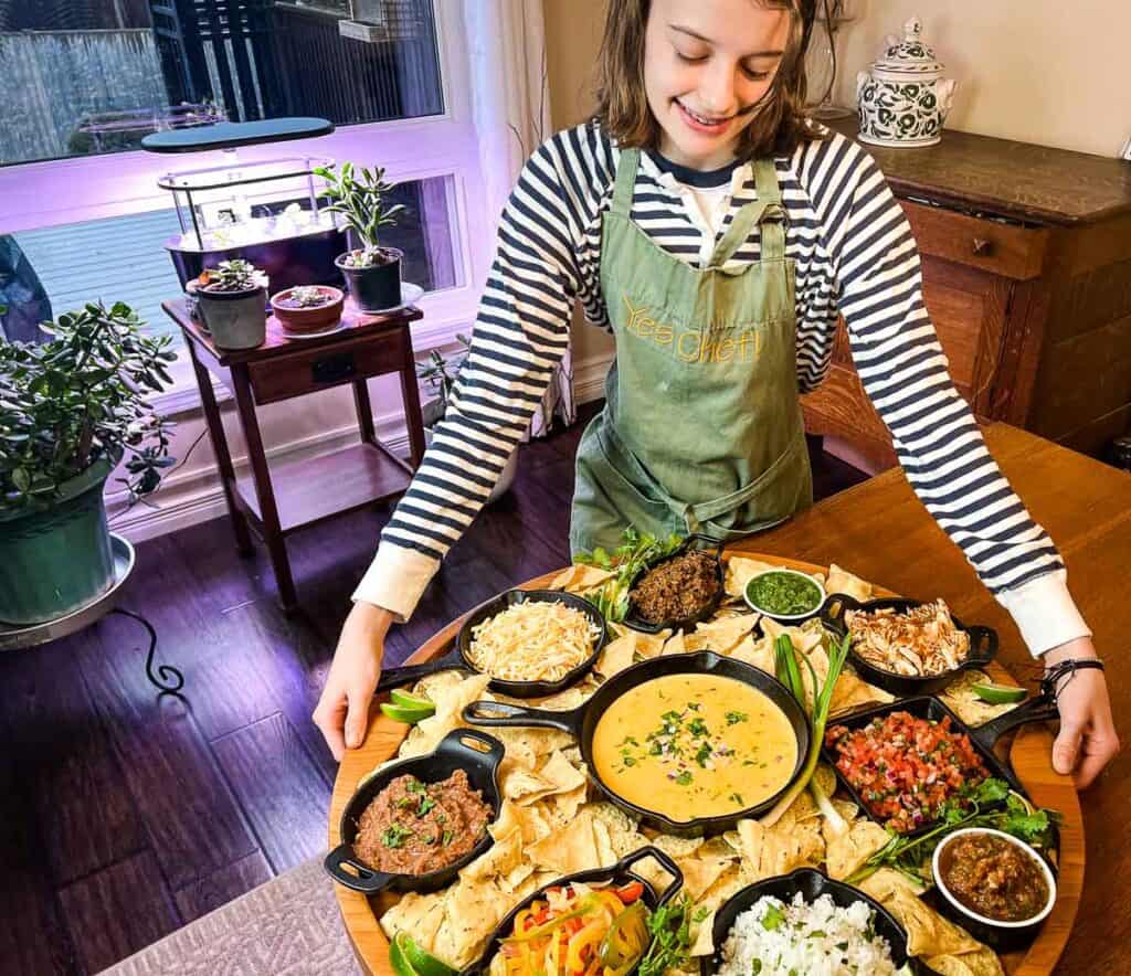 A woman in an apron standing in front of a large platter of food.