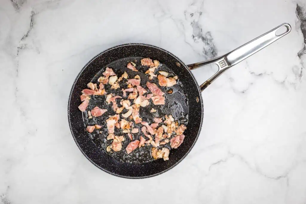Bacon in a frying pan on a marble surface.