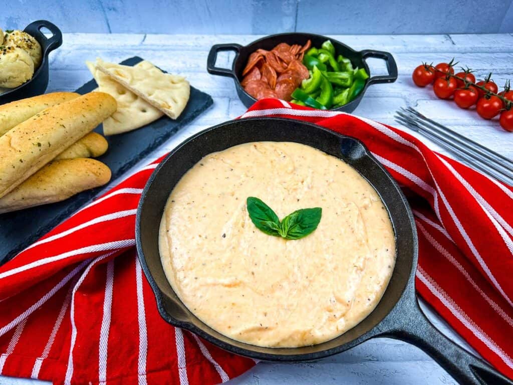 Cheesy dip in a skillet with bread and tomatoes.