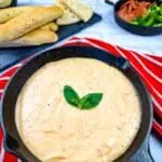 A skillet filled with Pizza fondue and bread on a red tablecloth.