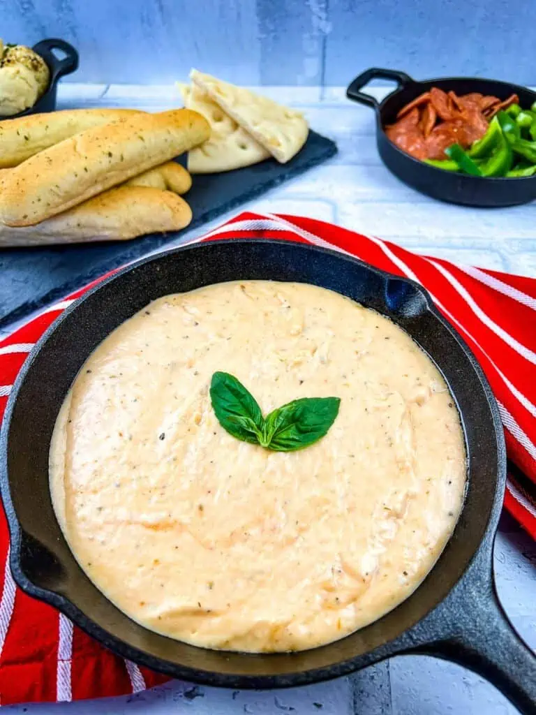 A skillet filled with Pizza fondue and bread on a red tablecloth.