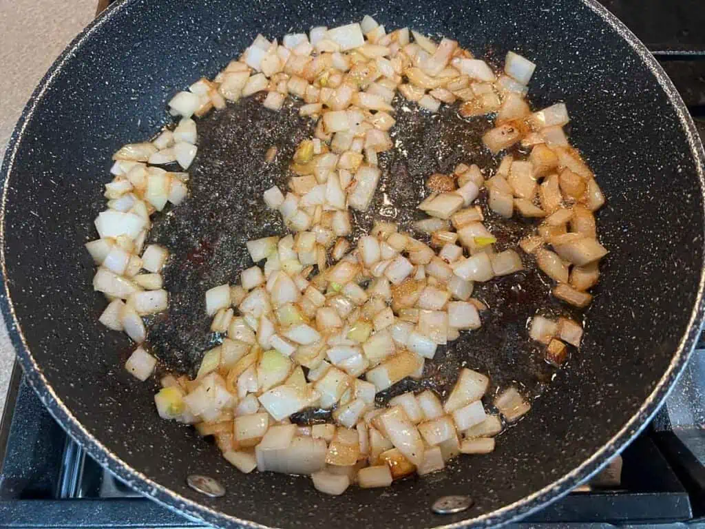 A frying pan full of chopped onions on a stove.