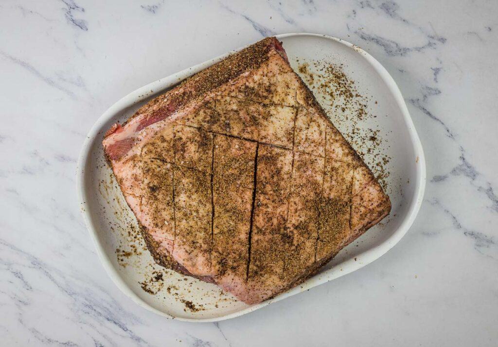 A piece of meat on a white plate with spices on it.