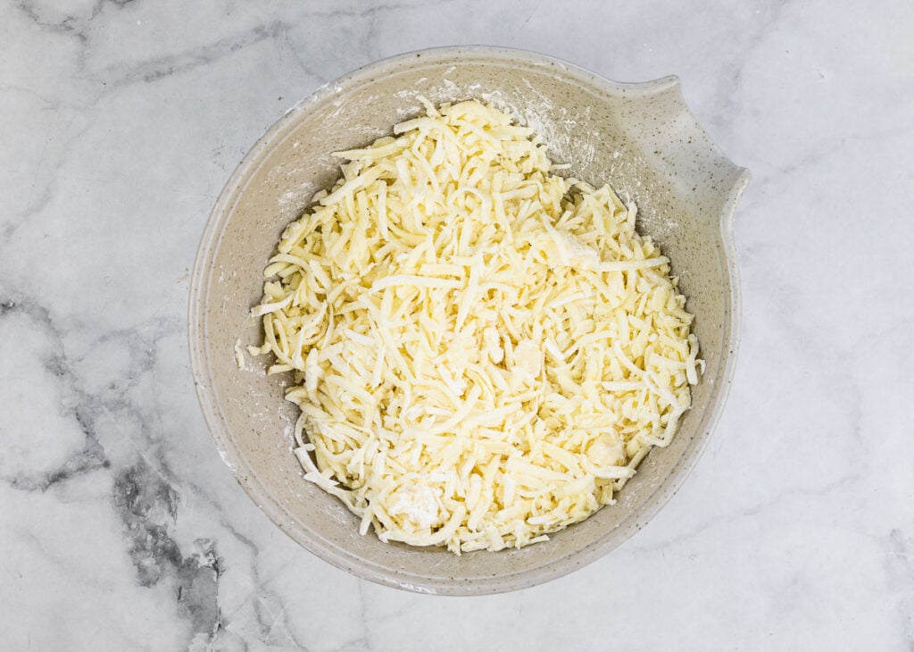 Shredded cheese in a bowl on a marble countertop.
