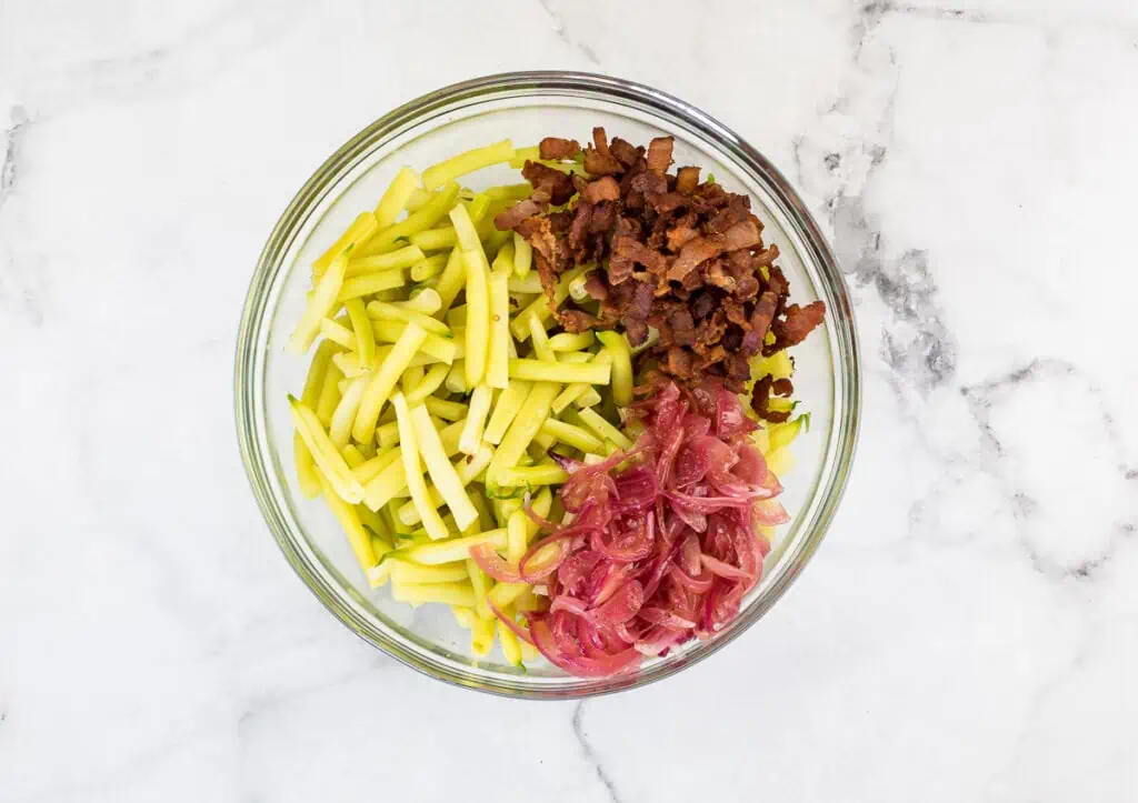 A bowl with onions, bacon, and zucchini in it.